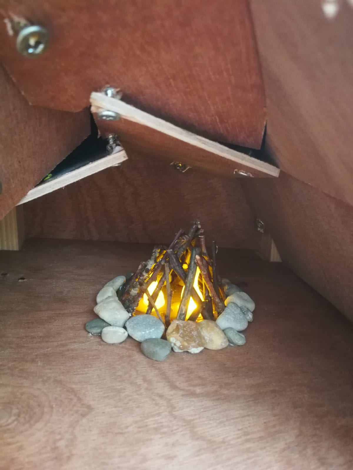 een mini-kampvuurtje met stokjes en kiezelsteentjes en een elektrisch lampje erin in een houten tentje